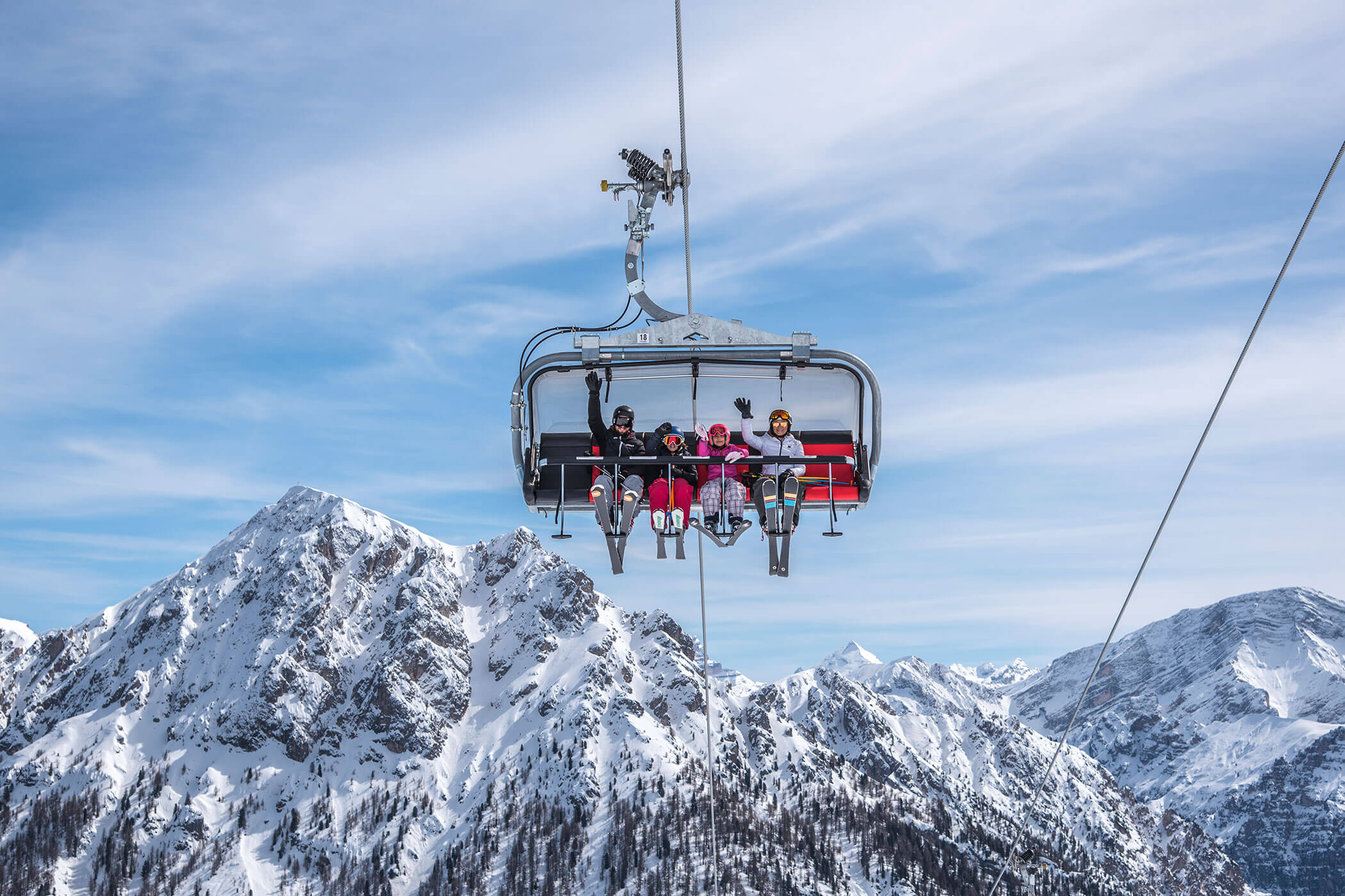 An einem klaren, sonnigen Tag fahren vier Personen mit einem Skilift über verschneite Berge. - Kerschbaumerhof
