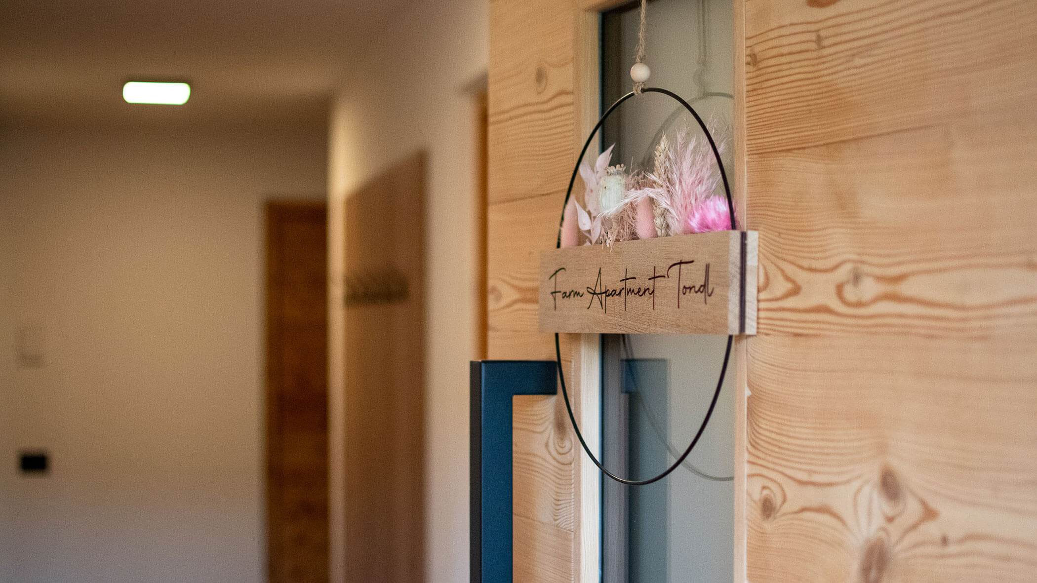 A modern wooden door with a circular floral sign hanging, reading Team Startpunkt Troisd. - Kerschbaumerhof