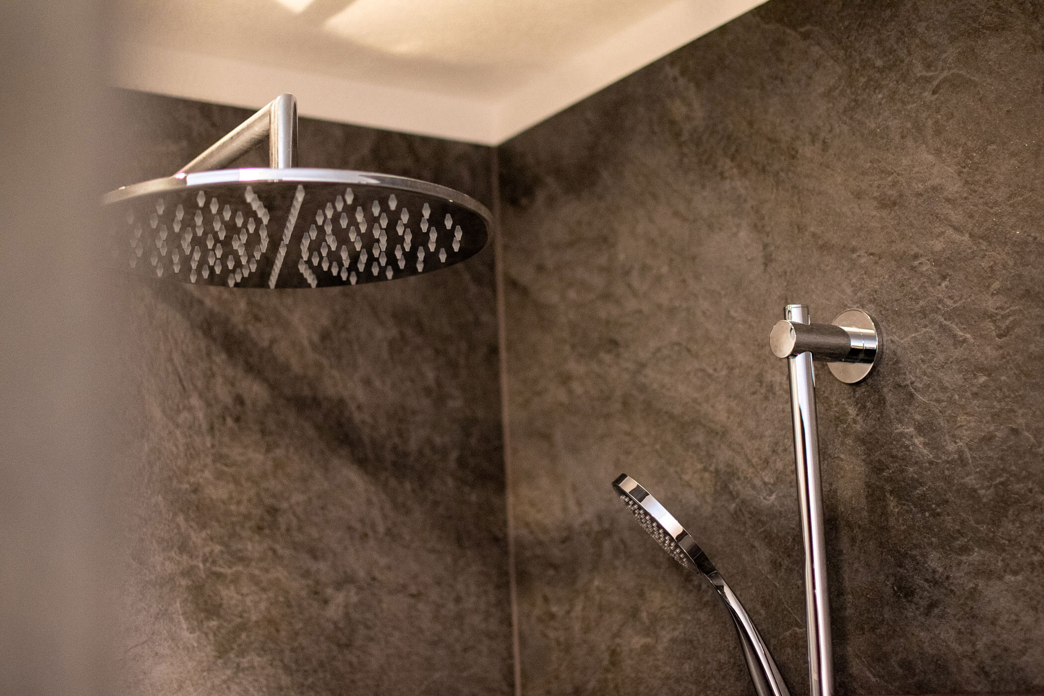 Moderne Dusche mit einer großen Regendusche und einer Handbrause vor dunklen Steinfliesen. - Kerschbaumerhof