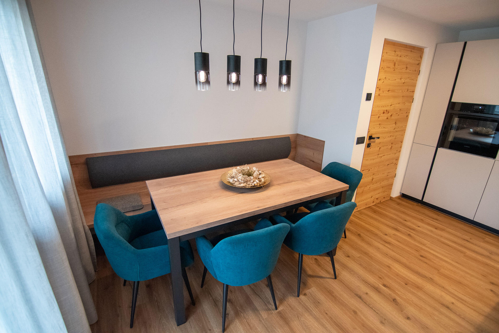 Moderner Essbereich mit Holztisch, tealfarbenen Stühlen, Sitzbank und vier Pendelleuchten darüber. - Kerschbaumerhof