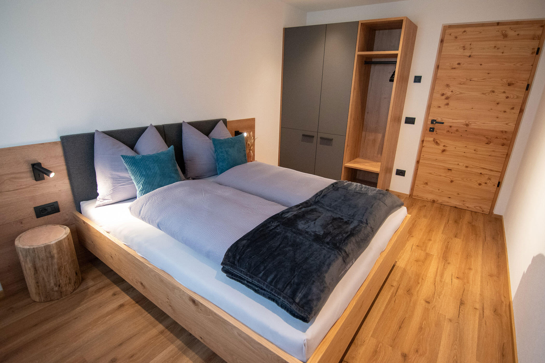 Modernes Schlafzimmer mit Holzfußboden, Doppelbett, grauer Bettwäsche, Kleiderschrank und natürlichen Holzakzenten. - Kerschbaumerhof